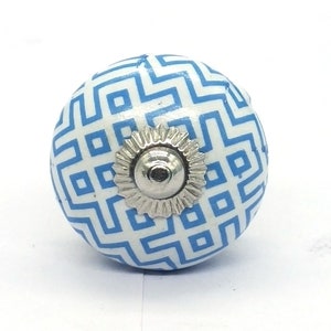 Puede incluir: Un pomo de armario redondo con un patrón geométrico azul y blanco. El pomo tiene una base de color plateado y un diseño decorativo. El pomo es un elemento decorativo para muebles y decoración del hogar.