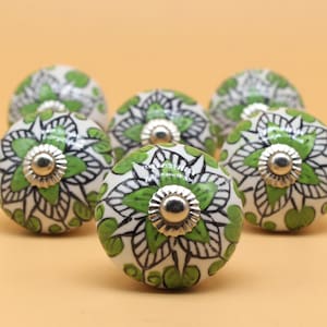 Peut inclure: Ensemble de boutons de meubles en céramique avec un motif floral. Les boutons sont blancs avec des détails peints en vert et noir. Chaque bouton a une base en métal argenté et une forme arrondie.