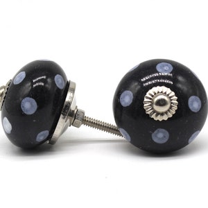 May include: Two black ceramic cabinet knobs with a white polka dot pattern. The knobs have a silver metal base and screw.