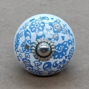 May include: A round, white ceramic cabinet knob with a blue floral pattern and a silver-colored metal base. The knob is approximately 1.5 inches in diameter, suitable for drawers or cabinets.