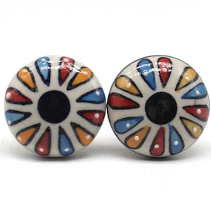 May include: Two ceramic knobs with a white background and a colorful floral design. The design features red, orange, blue, and yellow petals with white dots.