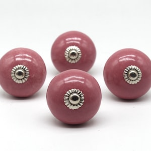 May include: Four pink ceramic cabinet knobs with silver accents. Each knob has a raised, circular design in the center.