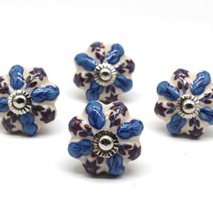 May include: Four ceramic cabinet knobs with a white base and blue and brown floral designs. Each knob has a silver metal center.