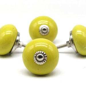 May include: Three yellow ceramic cabinet knobs with silver accents. The knobs are round and have a smooth, glossy finish.