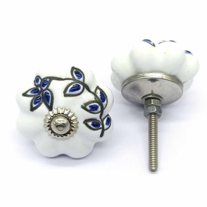 Puede incluir: Pomo de armario de cerámica blanca con un diseño floral azul y negro. El pomo tiene un tornillo plateado y una base plateada.