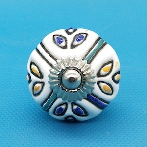 Könnte beinhalten: Weißer Keramik-Knopf mit einem blauen, grünen und gelben Blumendesign. Der Knopf hat eine silberne Metallmitte.