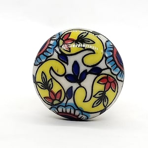 May include: A round ceramic knob with a yellow, blue, red, and white floral pattern.