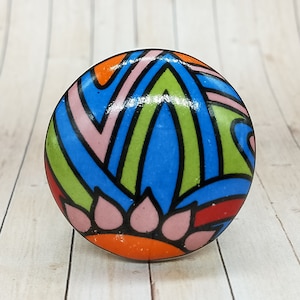 May include: A round cabinet knob featuring a glossy finish with a vibrant, multi-colored abstract pattern. The design includes bold black outlines filled with bright shades of blue, lime green, orange, and soft pink in a geometric floral motif.