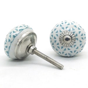 Puede incluir: Dos pomos de armario de cerámica blanca con un patrón geométrico turquesa. Los pomos tienen un tornillo de metal plateado y una base de metal plateado.