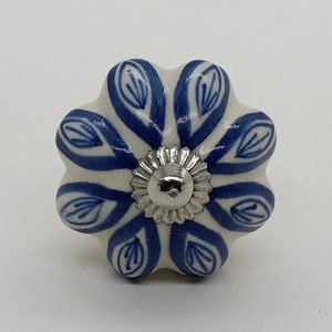 Op de afbeelding: Een witte keramische knop met een blauw bloemenmotief en een zilveren midden.