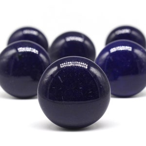 May include: A collection of seven dark blue, glossy spheres arranged against a white background. The spheres have a smooth, reflective surface, with highlights catching the light. The arrangement suggests a game or decorative item.