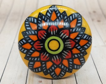 Peut inclure: Un bouton en céramique jaune avec un motif floral noir, orange et rouge.