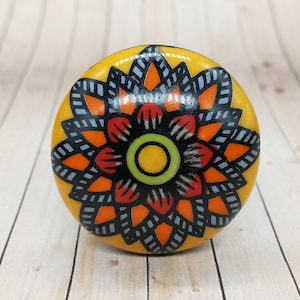 Puede incluir: Un pomo de cerámica amarillo con un diseño floral negro, naranja y rojo.