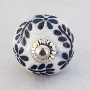 May include: White ceramic knob with a black floral design and a silver metal center.