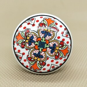 Peut inclure: Bouton de porte en céramique blanche avec un motif floral coloré. Le motif présente des fleurs rouges, orange, jaunes, bleues et vertes sur un fond blanc avec des pois rouges.