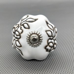 May include: White ceramic knob with a floral design in black. The knob has a silver metal centre.