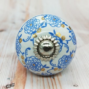 May include: White ceramic knob with a blue and gold floral design and a silver metal center.