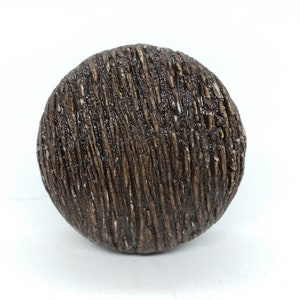 May include: A round, brown, wooden knob with a textured surface.