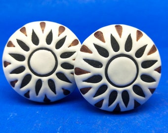 May include: Two white ceramic knobs with a black and brown sunburst design. The knobs are round and have a raised design.