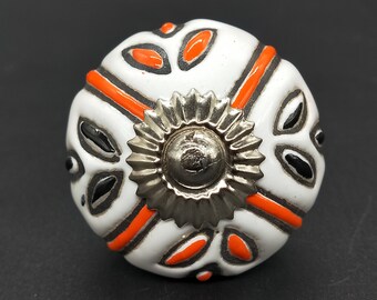 May include: White ceramic knob with an orange and black geometric design and a silver metal center.