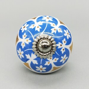 以下が含まれることがあります： 金色の花の模様と銀色の金属の中心部を持つ、青と白のセラミック製のノブです。