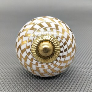Peut inclure: Bouton de porte en céramique blanche avec un motif chevron doré et un centre en métal doré.
