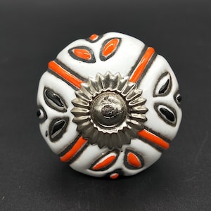 Pode incluir: Botão de cerâmica branco com um design geométrico laranja e preto e um centro de metal prateado.
