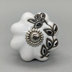 Peut inclure: Bouton de porte en céramique blanche avec un motif floral noir et un centre en métal argenté.