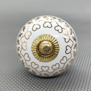 May include: White ceramic knob with a gold heart pattern and a gold metal center.