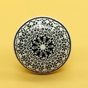 Könnte beinhalten: Weißer Keramik-Knopf mit einem schwarz-weißen Blumendesign.