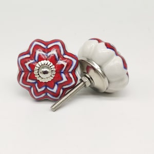 May include: Two ceramic drawer knobs with a white base and red and blue striped designs. One knob has a silver screw and the other has a silver base.