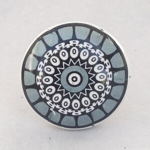 Könnte beinhalten: Ein runder Keramik-Knopf mit einem geometrischen Muster in Grau und Weiß. Der Knopf hat ein kreisförmiges Muster mit einer zentralen augenartigen Form.
