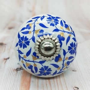 May include: White ceramic knob with a blue and gold floral pattern. The knob has a silver metal center.
