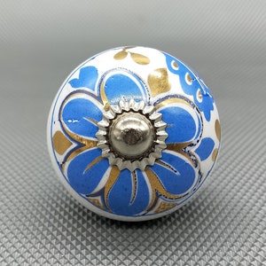 以下が含まれることがあります： 青と金のフローラルデザインが施された白いセラミックノブ。ノブの中央は銀色の金属製です。