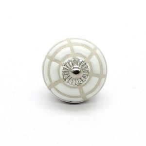 May include: White ceramic knob with a geometric pattern and a silver metal centre.