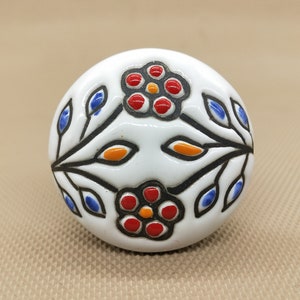 Könnte beinhalten: Weißer Keramik-Knopf mit floralem Design. Die Blumen sind rot, orange und blau mit schwarzen Umrissen.