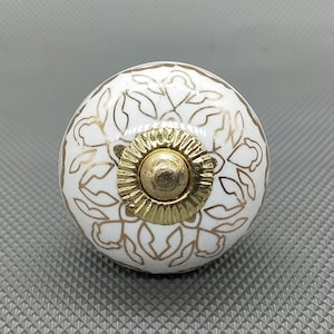 Op de afbeelding: Witte keramische knop met een gouden bloemmotief en een gouden metalen centrum.