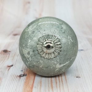May include: A round, silver-colored cabinet knob with a distressed, light green finish. The knob has a decorative, circular design around the center.