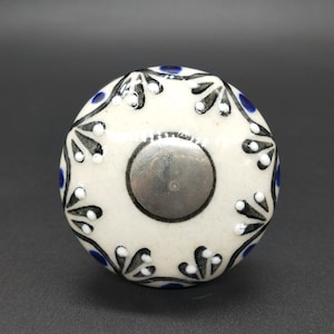 Op de afbeelding: Witte keramische knop met een blauw en zwart bloemenontwerp. De knop heeft een zilveren midden.