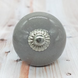 May include: A gray ceramic knob with a silver decorative trim. The knob is round and has a smooth surface.