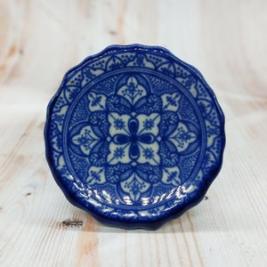 Może przedstawiać: Ceramiczny gałka w kolorze niebieskim i białym z ozdobnym, skomplikowanym wzorem. Gałka ma falisty brzeg i błyszczące wykończenie.