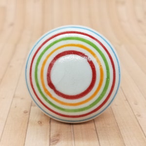 May include: A white ceramic knob with a colorful concentric circle design. The circles are red, orange, yellow, green, and blue.