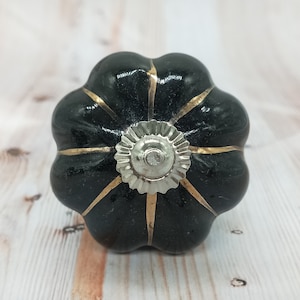 Peut inclure: Bouton de porte en céramique noire en forme de citrouille avec des accents dorés et un centre argenté.