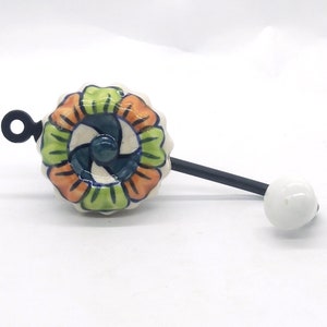 Könnte beinhalten: Ein Keramikhaken mit einem floralen Design in Grün-, Orange- und Blautönen. Der Haken ist an einer schwarzen Metallstange befestigt, an deren Ende sich eine weiße Keramik Kugel befindet.