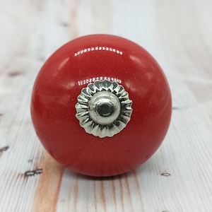 Könnte beinhalten: Roter Keramik-Schrankknopf mit einem silbernen, dekorativen Metallaccent.