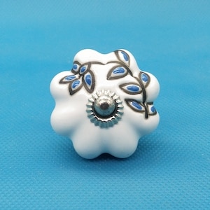 Puede incluir: Pomo de cerámica blanco con un diseño floral azul y negro. El pomo tiene un centro de metal plateado.