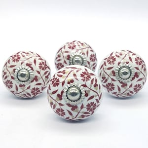 Könnte beinhalten: Vier weiße Keramikknöpfe mit rotem Blumenmuster und silbernen Akzenten. Die Knöpfe sind rund und haben ein erhabenes Design.