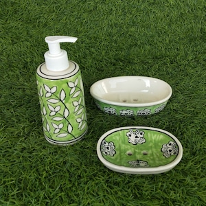 Puede incluir: Un juego de baño de cerámica verde y blanco con un dispensador de jabón y dos jaboneras. El dispensador de jabón tiene una bomba blanca y un diseño floral. Las jaboneras son ovaladas y tienen un diseño floral.