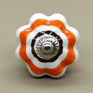 May include: A white ceramic knob with orange and brown stripes. The knob has a silver metal center.