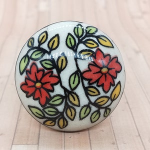 May include: White ceramic knob with a floral design. The knob features red and orange flowers with green leaves and black outlines.
